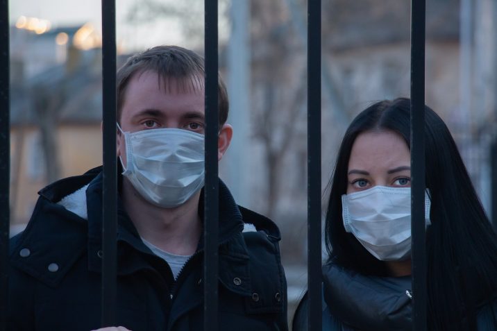 A man and woman with masks behind bars