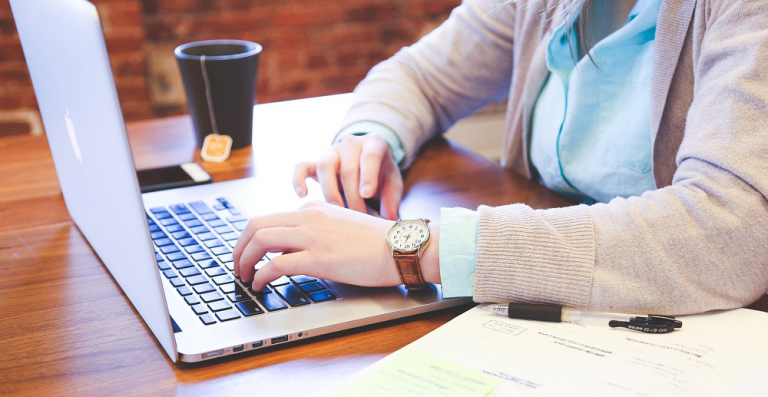person typing on a laptop that is placed on a wooden table