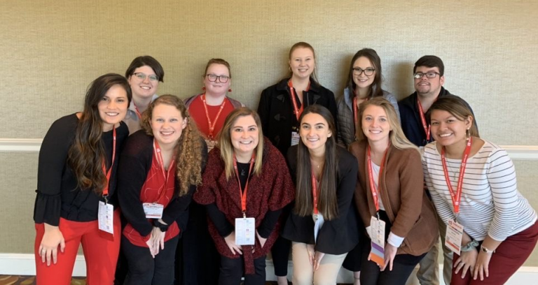 11 students posing for a photo at a conference