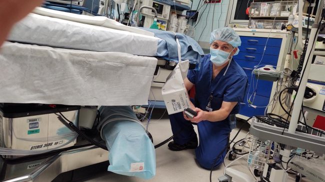 Man in scrubs and mask near hospital bedside