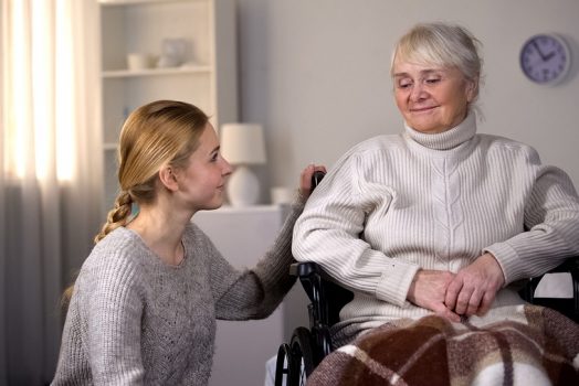 Young woman kneeling next to older woman in wheelchair