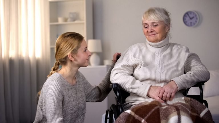 Young woman kneeling next to older woman in wheelchair