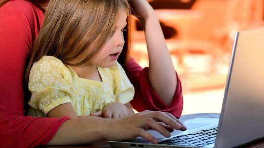 A little girl sitting on her mother's lap while looking at a computer.