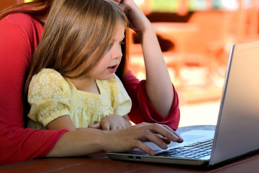 A little girl sitting on her mother's lap while looking at a computer.