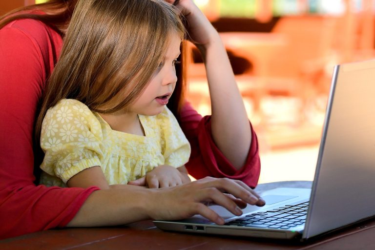 A little girl sitting on her mother's lap while looking at a computer.