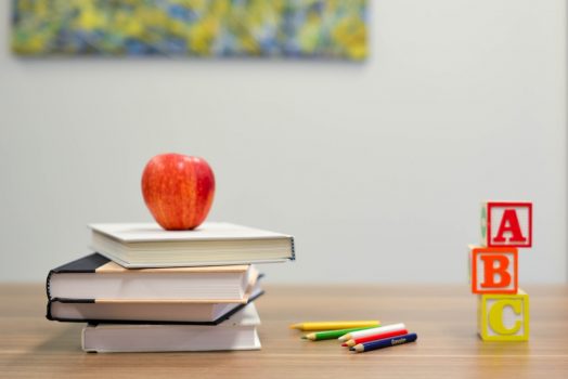 A photo of an apple on top of books next to letters.