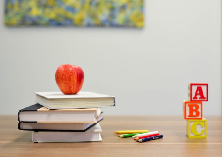 A photo of an apple on top of books next to letters.