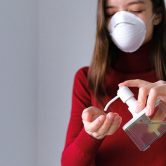 Woman in mask using hand sanitizer