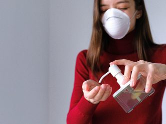 Woman in mask using hand sanitizer