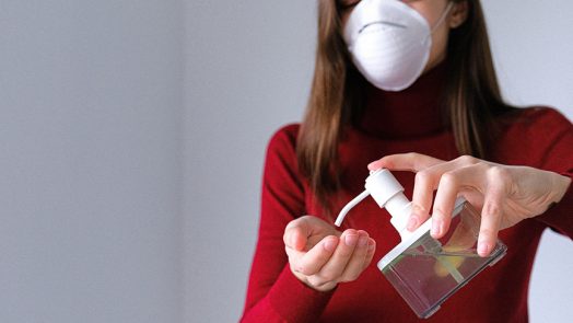 Woman in mask using hand sanitizer