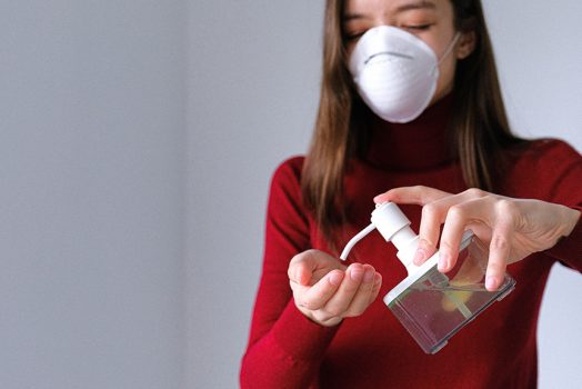 Woman in mask using hand sanitizer