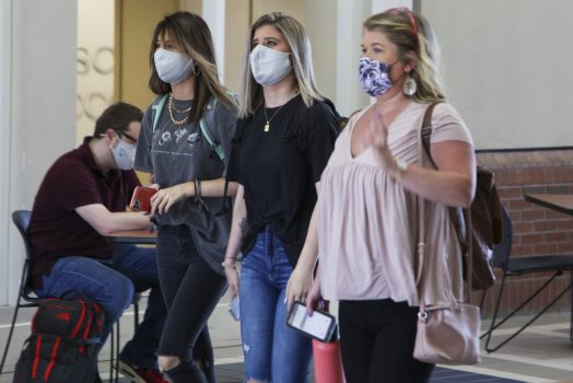 Three female college students walking wearing face masks.