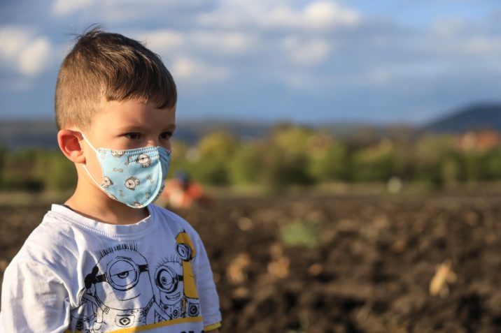 Small boy wearing a face mask while standing outside.