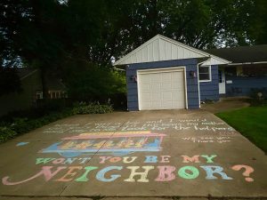 Chalk drawing of a trolley. Caption: "When I was a boy and I would see scary things in the news, my mother would say to me, 'Look for the helpers.' - Fred Rogers. Wee see you. Thank you." Underneath the trolley drawing, the caption: "WON'T YOU BE MY NEIGHBOR?" 