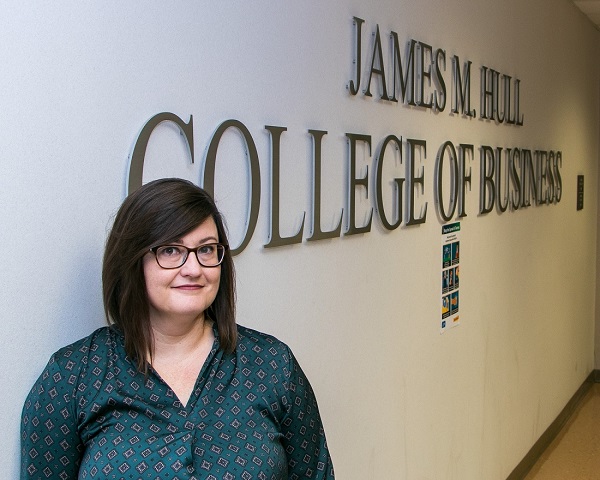 woman stands in front of James M. Hull College of Business wall sign