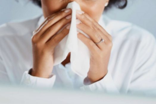 Woman sneezing into tissue.