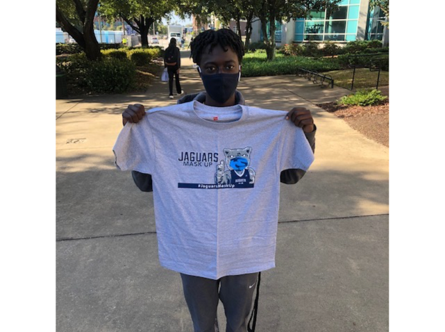 masked student holds up grey Jaguars Mask Up T-shirt