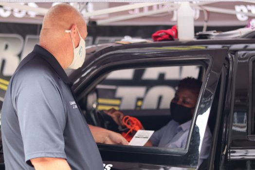 Police officer wearing face mask hands a piece of paper to a driver behind the wheel of a black car