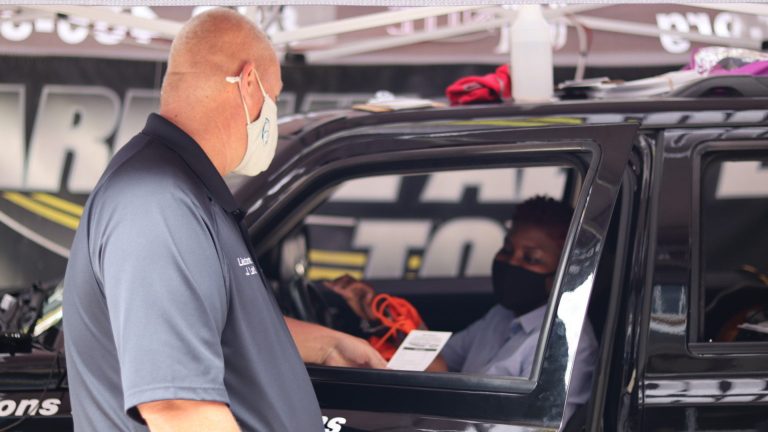 Police officer wearing face mask hands a piece of paper to a driver behind the wheel of a black car