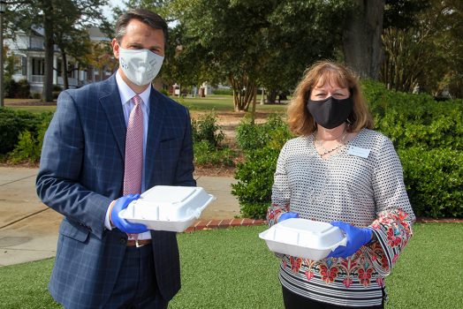 Man and woman in masks holding to go plates