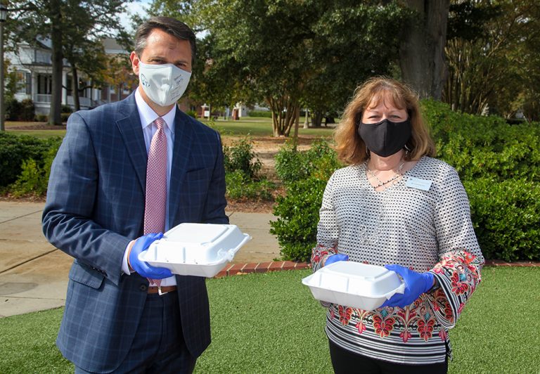 Man and woman in masks holding to go plates