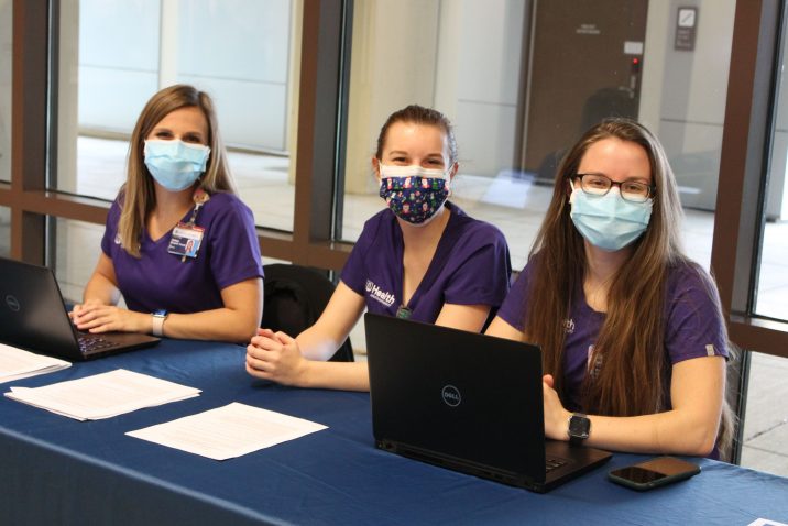 Three ladies in scrubs with masks on sitting behind a table.