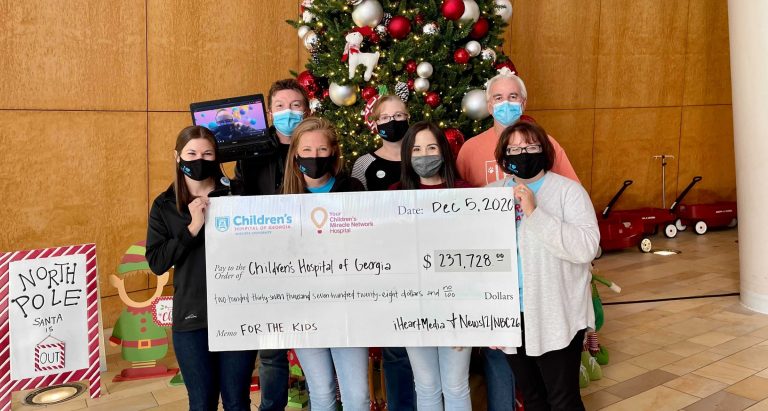 people with giant check in front of Christmas tree