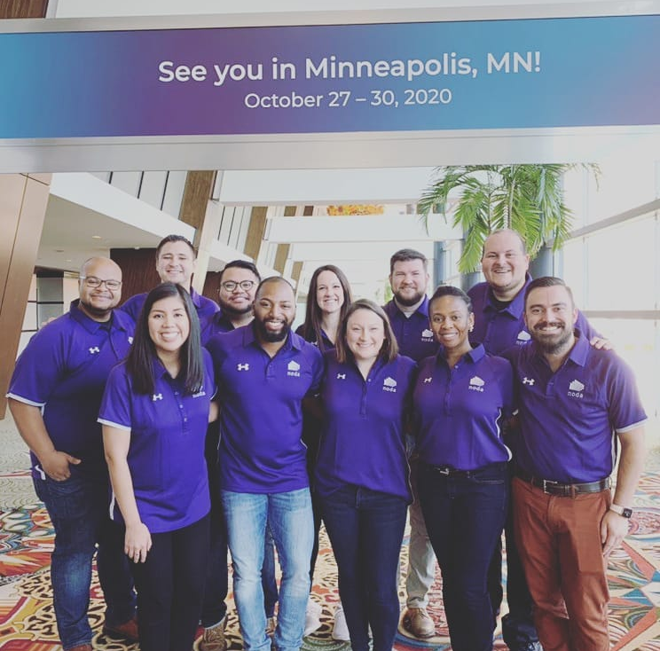 11 men and women in purple collared shirts smile for a photo