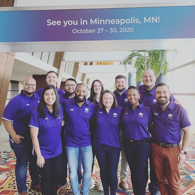 11 men and women in purple collared shirts smile for a photo