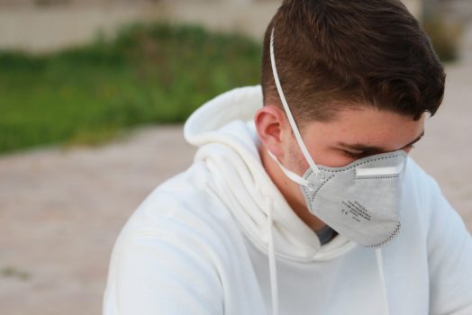 A man sitting down with a white shirt and a mask on.