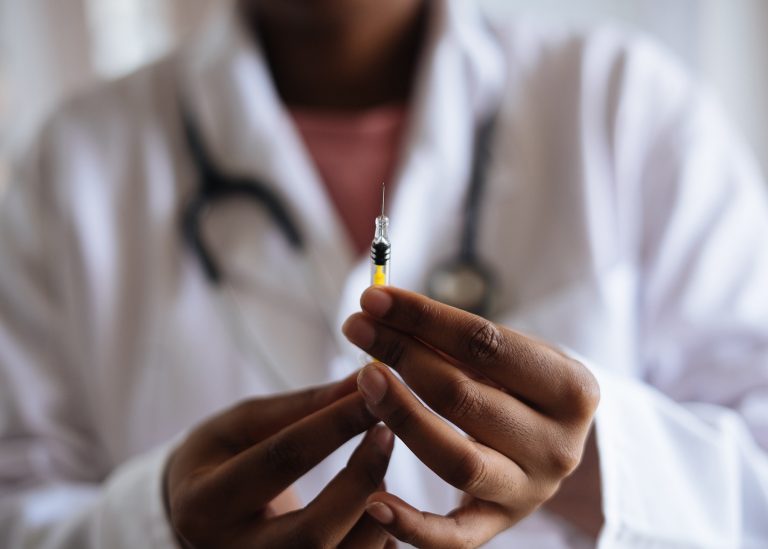 A person in a lab coat holding a needle.
