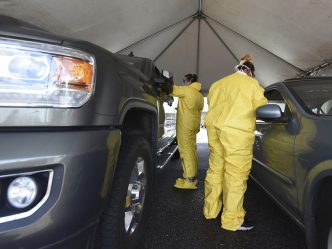 Two workers in PPE testing patients inside cars