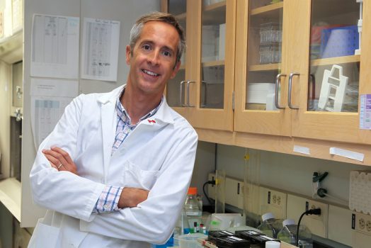 Dr. Eric Belin de Chantemele, in a white lab coat, leans next to a counter in his lab