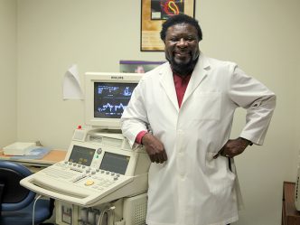 Dr. Gaston Kapuku, in white lab coat, stands in front of lab equipment