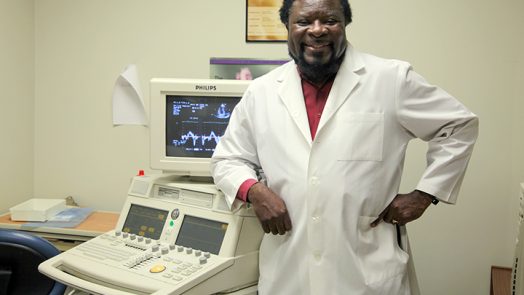 Dr. Gaston Kapuku, in white lab coat, stands in front of lab equipment