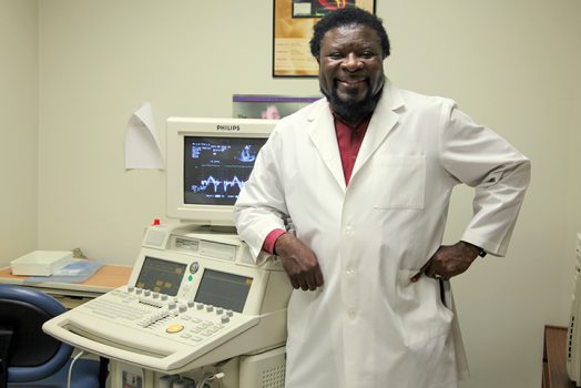 Dr. Gaston Kapuku, in white lab coat, stands in front of lab equipment