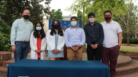 Six people, all wearing masked, stand behind a table with a tablecloth that reads "Student Government Association"