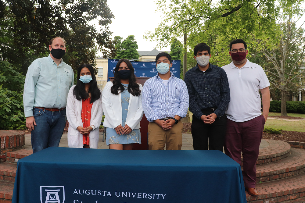 Six people, all wearing masked, stand behind a table with a tablecloth that reads "Student Government Association"
