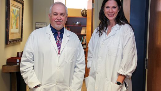 Drs. David Step (on left) and Jennifer Sullivan stand in hallway in white lab coats