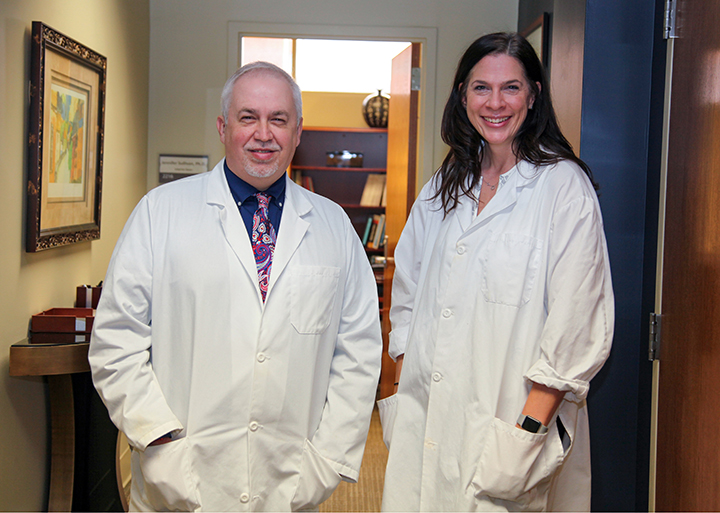 a man and a woman stand in hallway in white lab coats