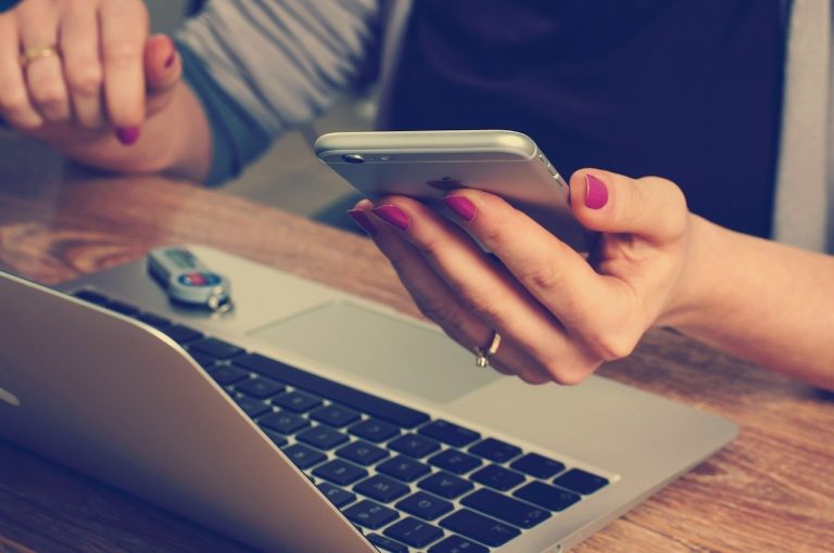 Woman holding a phone over the computer.