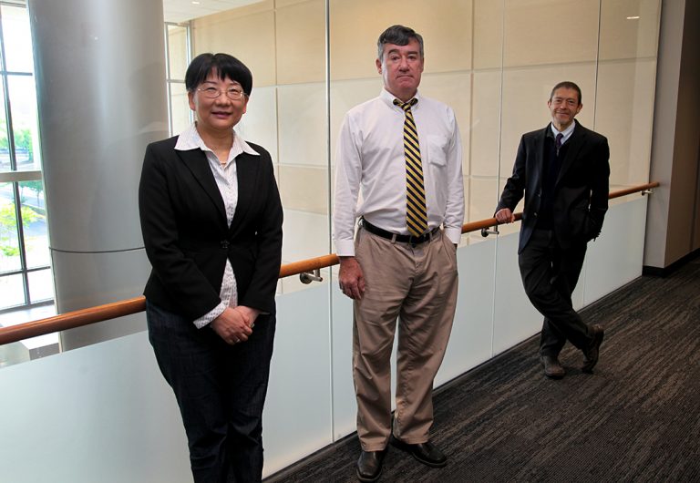 A woman and two men stand in a line looking at the camera