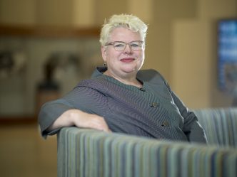 Woman with short blonde hair sits on couch with arm on back
