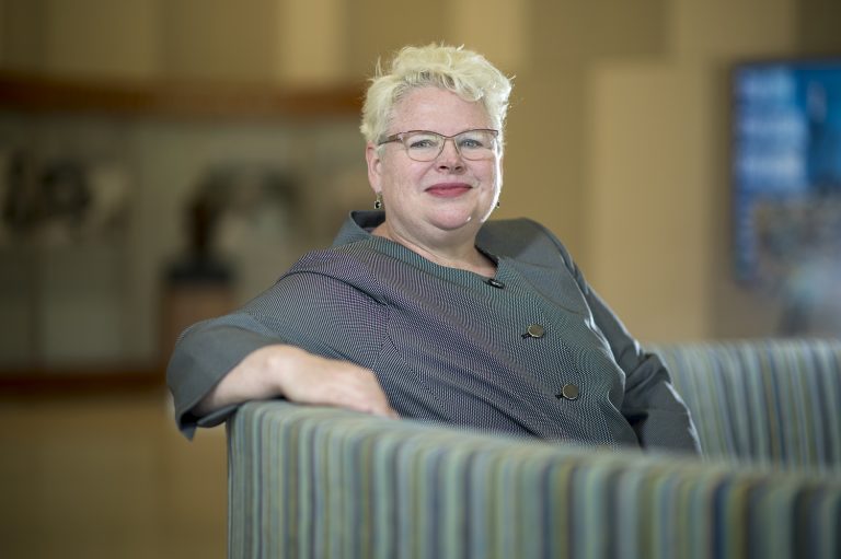 Woman with short blonde hair sits on couch with arm on back