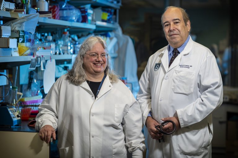 Woman in white coat stands next to man in white coat in laboratory setting