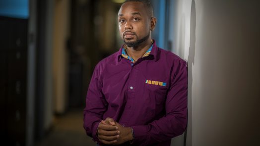 Young African American man in purple shirt stands in hallway looking at camera