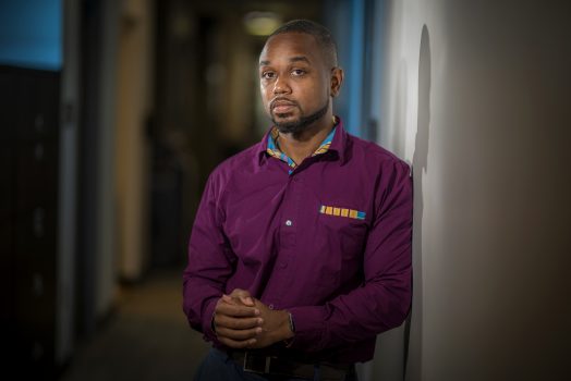 Young African American man in purple shirt stands in hallway looking at camera