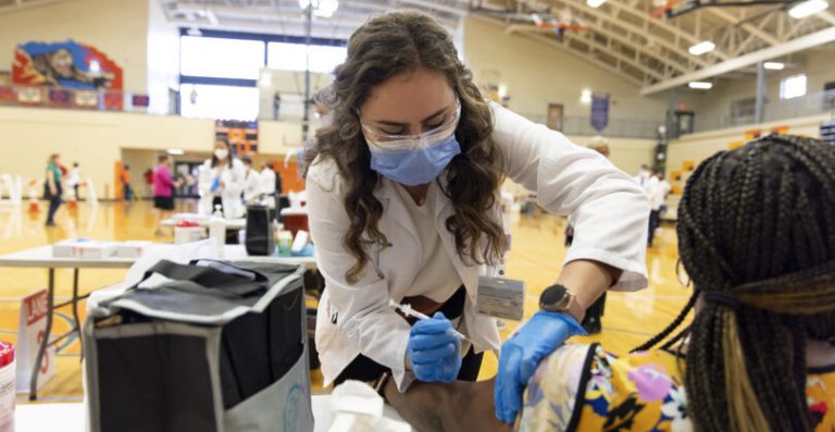 woman administers a shot to a woman's left arm