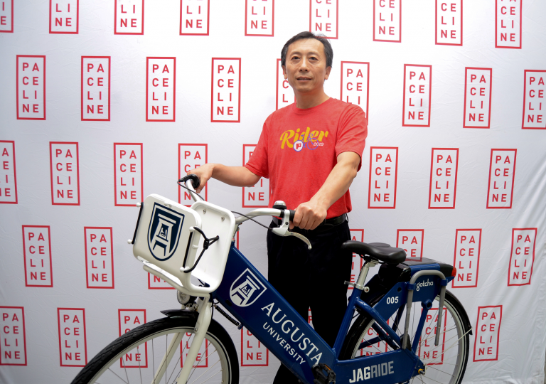a man wearing a red T-shirt holds a blue and white bike