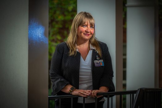 Woman in navy blazer stands in front of building with hands crossed